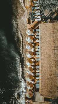 Stunning aerial view of a tropical beach resort with umbrellas and waves along the shoreline.