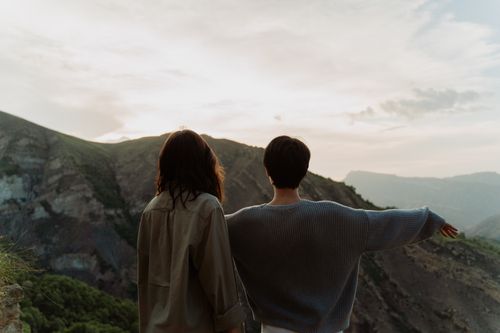Free Two friends enjoy a serene sunset view over mountains, capturing a moment of tranquility and connection. Stock Photo