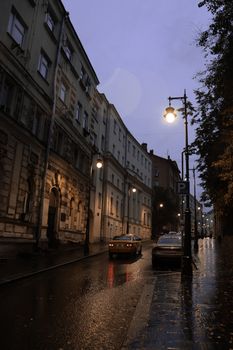 Atmospheric street view at twilight with rainy weather and parked cars, enhancing the urban mood.