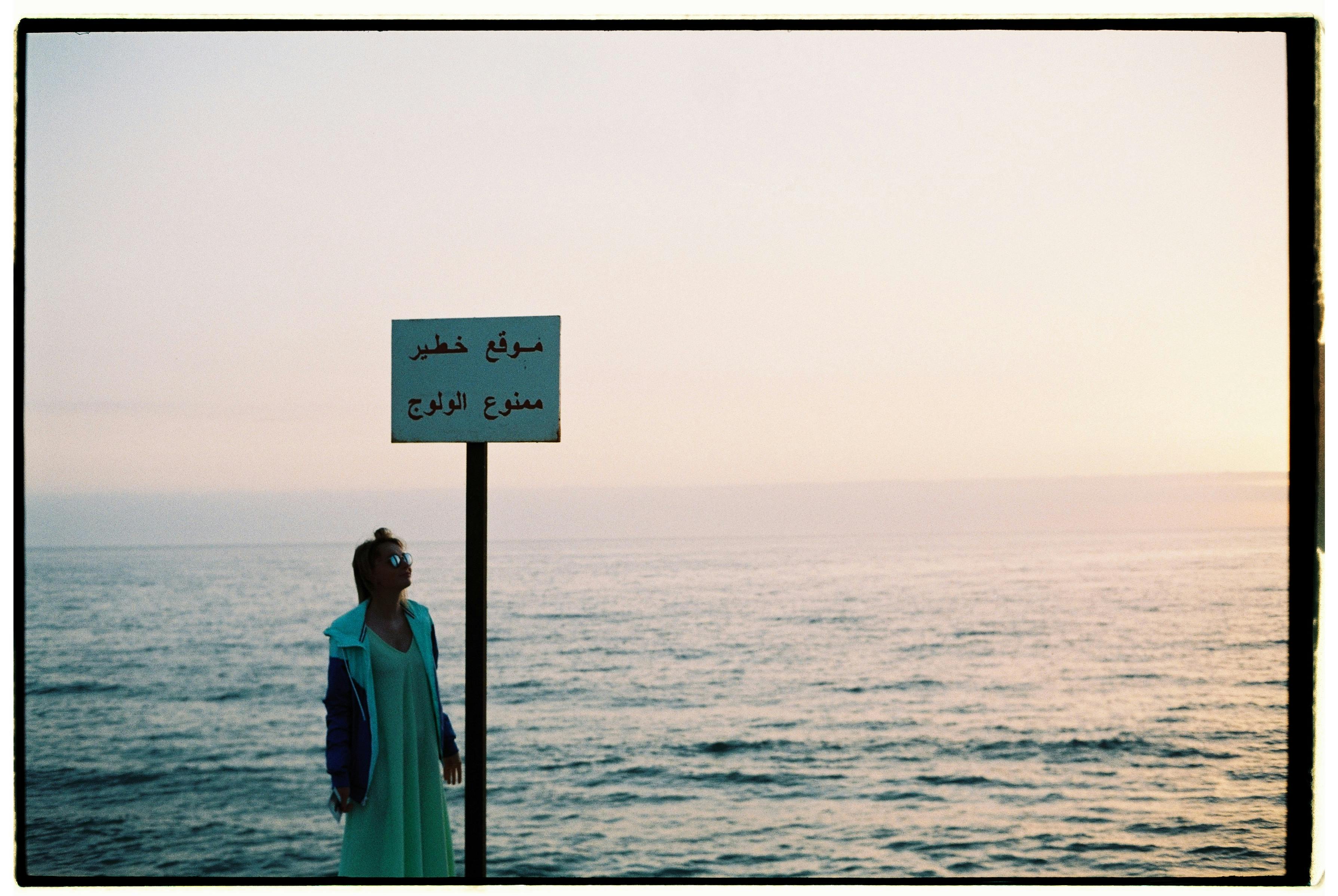 Woman standing by the sea with sign in Morocco during sunset.