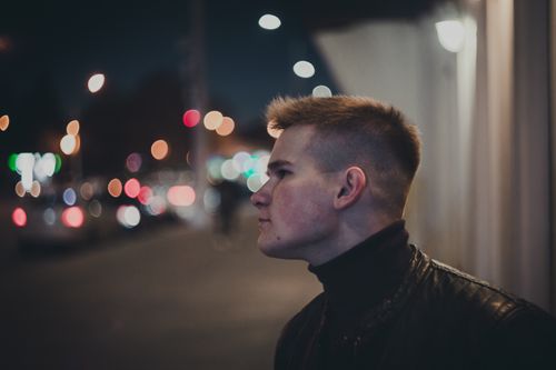 Free Side profile of a man in a leather jacket against a city night backdrop. Blurred bokeh lights enhance the modern urban feel. Stock Photo