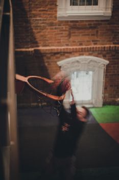 Blurred motion of a man dunking a basketball indoors, capturing dynamic sports action.