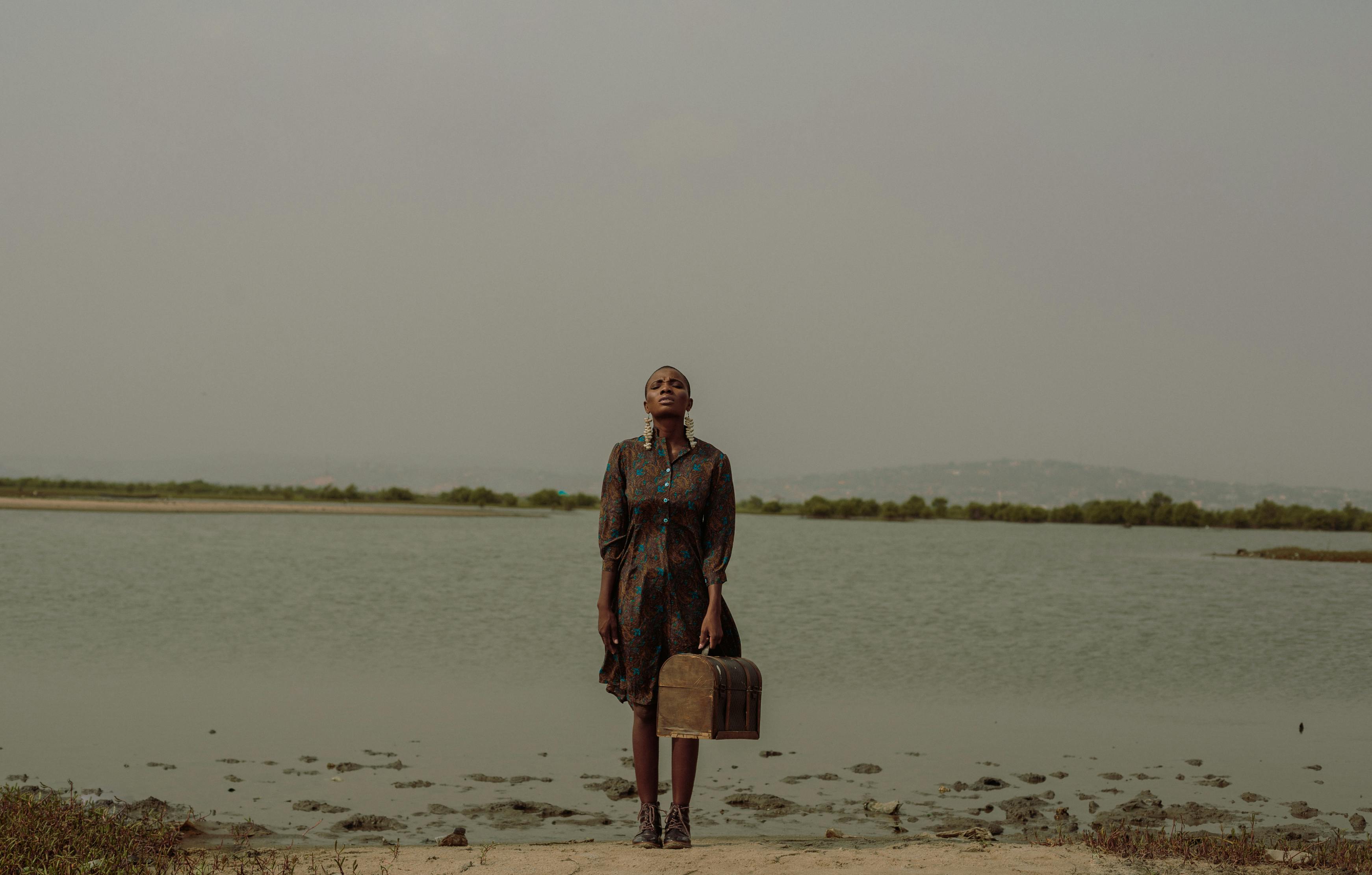 Woman in a printed dress poses elegantly by a lakeside in Accra, Ghana, exuding grace.
