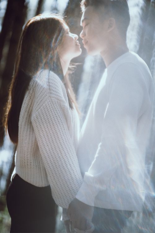 Free A romantic couple in a warm embrace standing in a sunlit forest, creating a dreamy atmosphere. Stock Photo