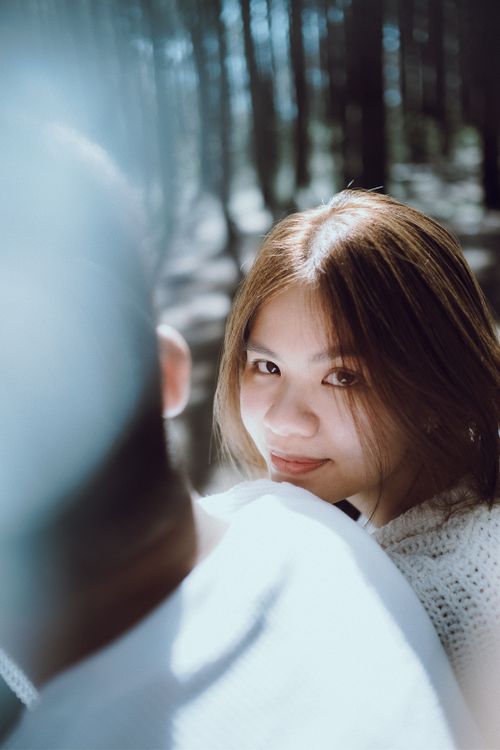 Free Smiling young woman gazing back in a sunlit forest, capturing a warm, serene moment. Stock Photo