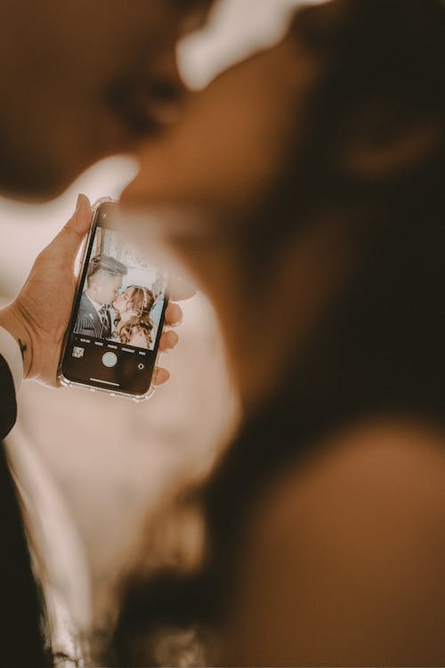 Hand Holding Cellphone with Picture of Woman and Man Kissing