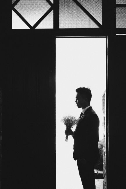 A groom holding a bouquet silhouetted against a doorway, symbolizing love and anticipation.
