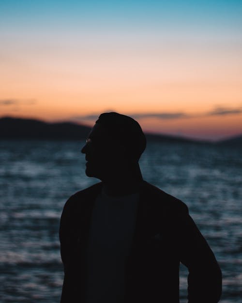 Silhouette of Man Standing Near Body of Water during Sunset