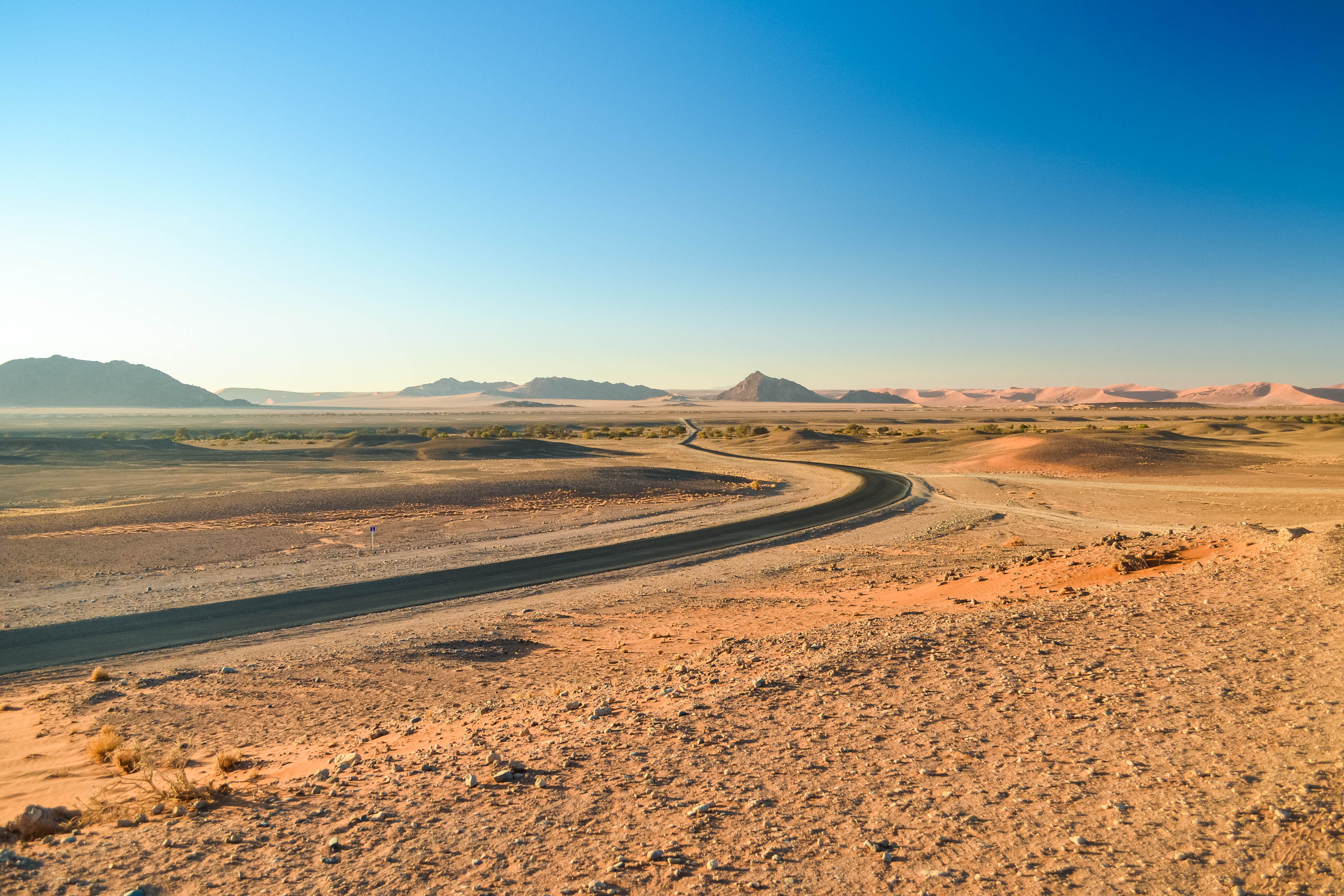 A winding road through the vast Namib Desert landscape under a clear blue sky.