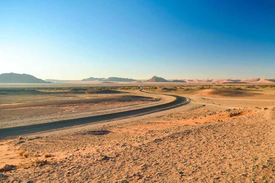 A winding road through the vast Namib Desert landscape under a clear blue sky.