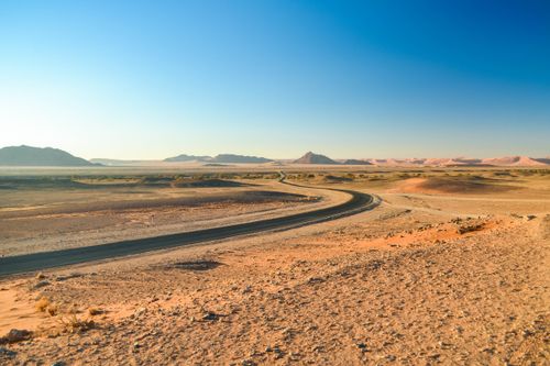 Free A winding road through the vast Namib Desert landscape under a clear blue sky. Stock Photo