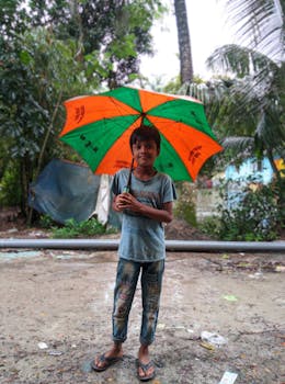 A cheerful boy holding a vibrant umbrella outdoors in Bangladesh.