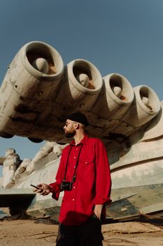 Man in red shirt exploring a large abandoned aircraft in a desert setting during the day.