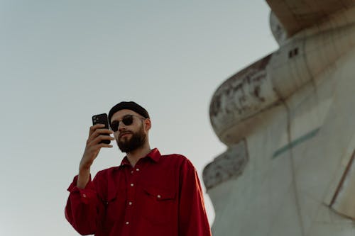 A Man in Red Long Sleeves and Beanie Holding His Mobile Phone