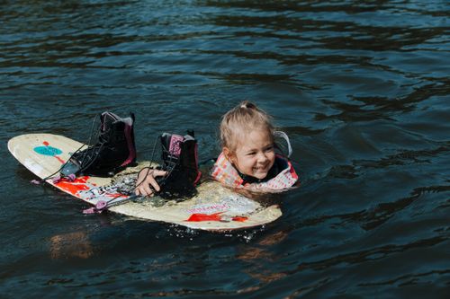 Free A young girl in a life jacket enjoys wakeboarding on a sunny day in the water. Stock Photo