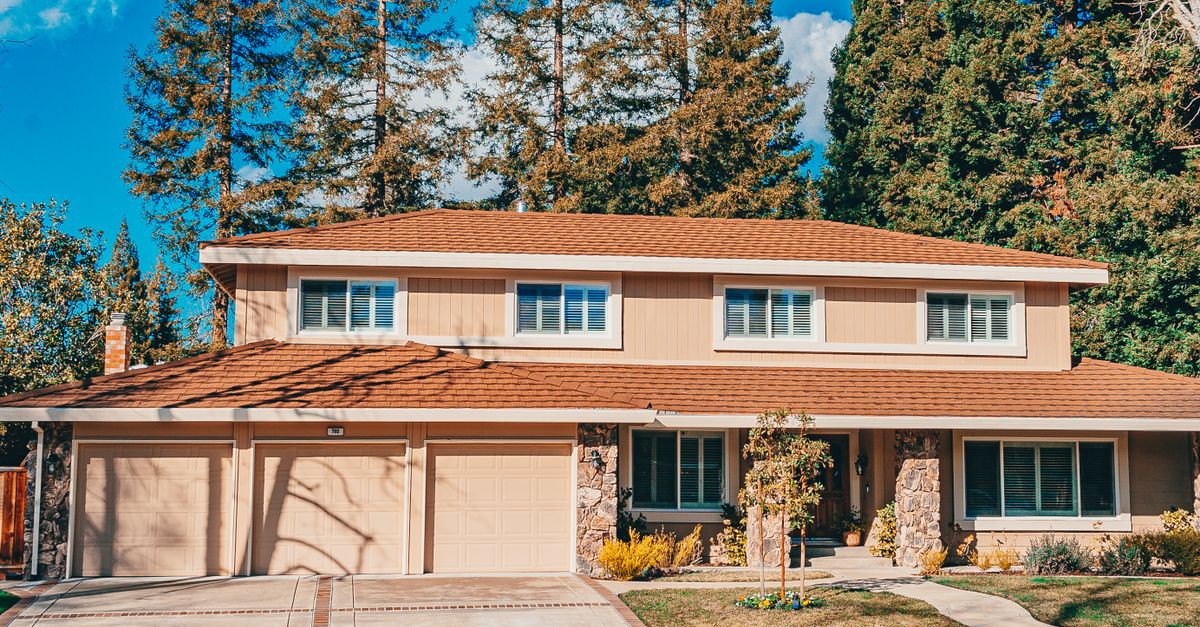 Charming two-story house with a landscaped front yard and wide driveway under clear blue skies.