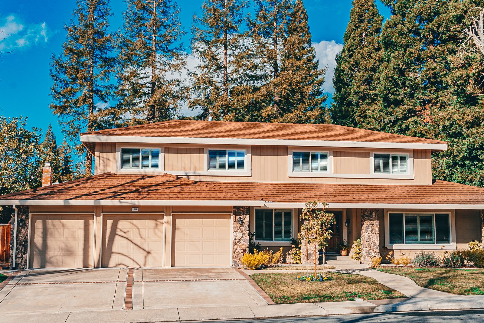 A two-storey house with a wide driveway and landscaped front yard under a clear sky.