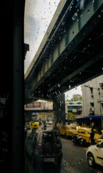 Raindrops on window reveal busy urban street scene beneath an overpass.