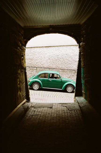 A green Volkswagen Beetle parked in an urban tunnel, exuding vintage vibes.