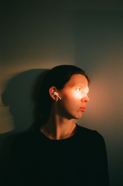 A moody portrait of a woman with earphones in sunlight creating an artistic shadow play.