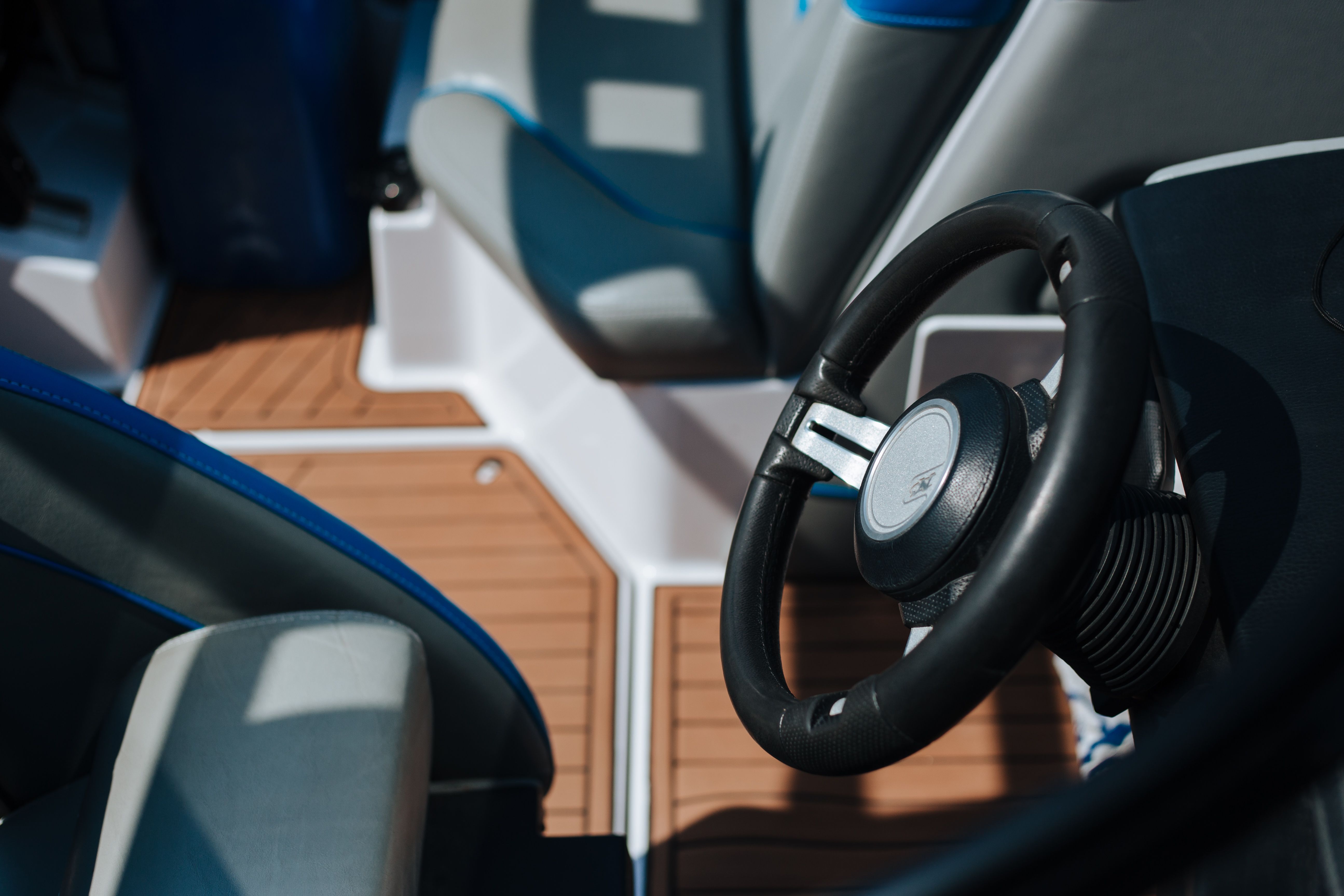 Detailed view of a boat's steering wheel and deck seating under sunlight outdoors.