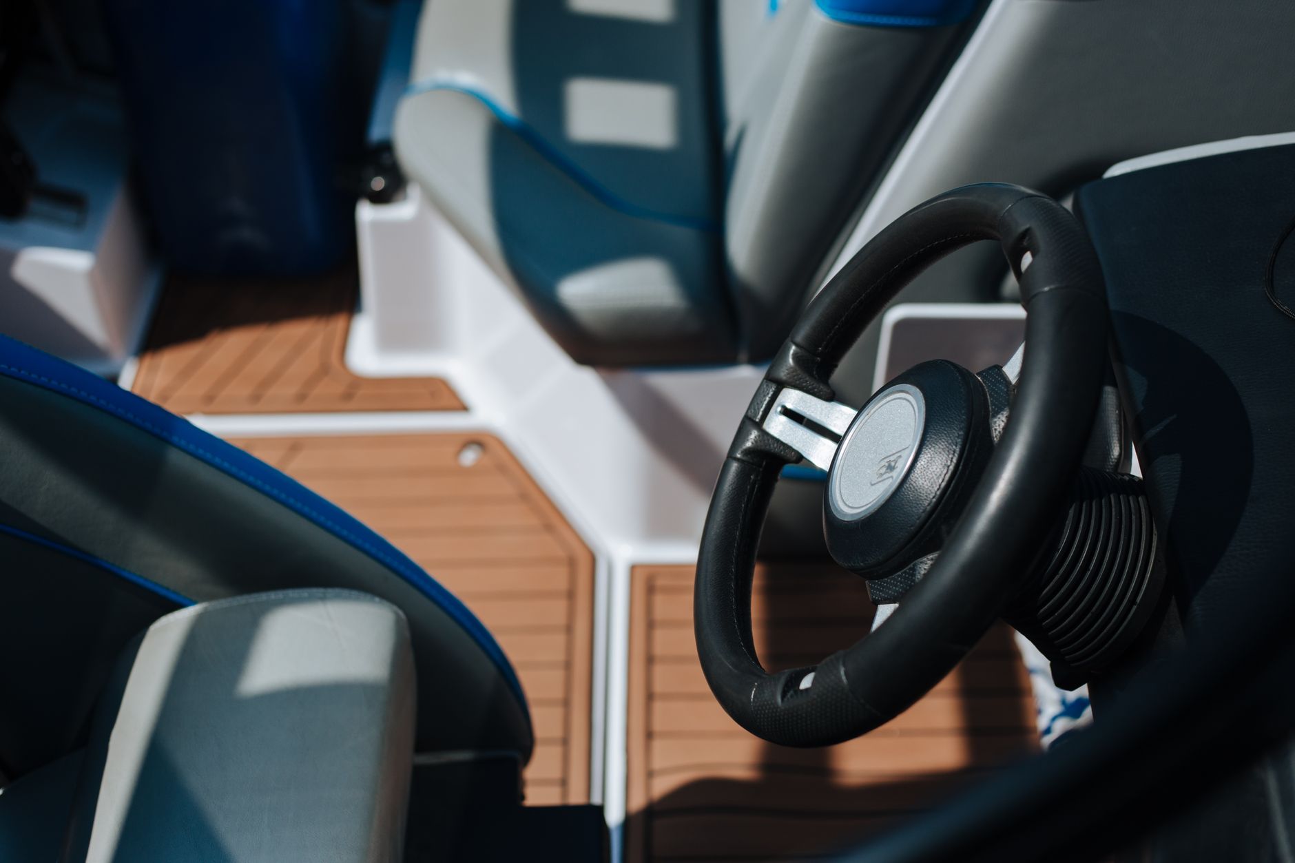 Detailed view of a boat's steering wheel and deck seating under sunlight outdoors.