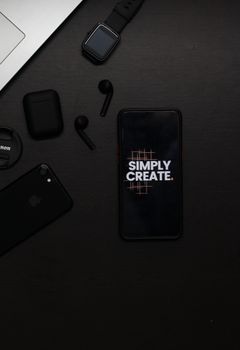 Black flat lay of gadgets including smartphone with 'Simply Create' text, smartwatch, and stylish earpieces.