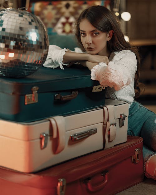 A Woman in White Long Sleeves Sitting Beside the Luggage with Disco Ball on Top