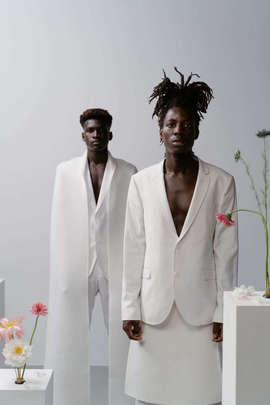 Two men in white suits with floral detailing in a studio fashion shoot