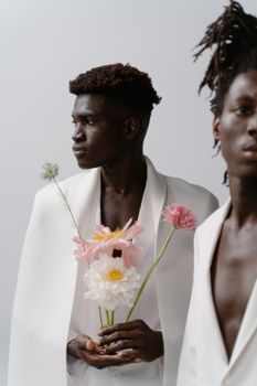 Stylish African American men in white blazers holding pastel flowers on a white background.