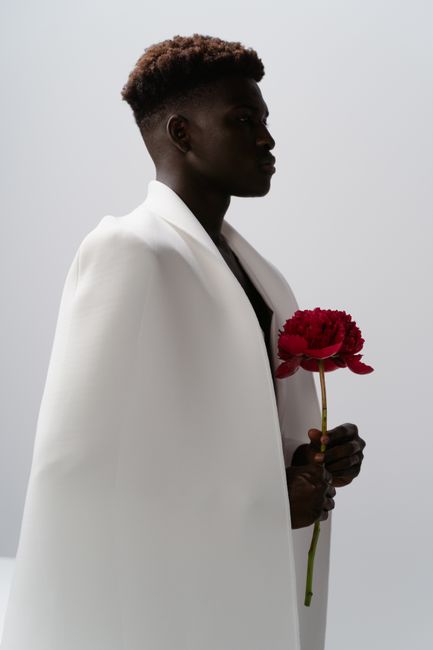 Stylish African man in white fabric holding a red peony against a studio background.