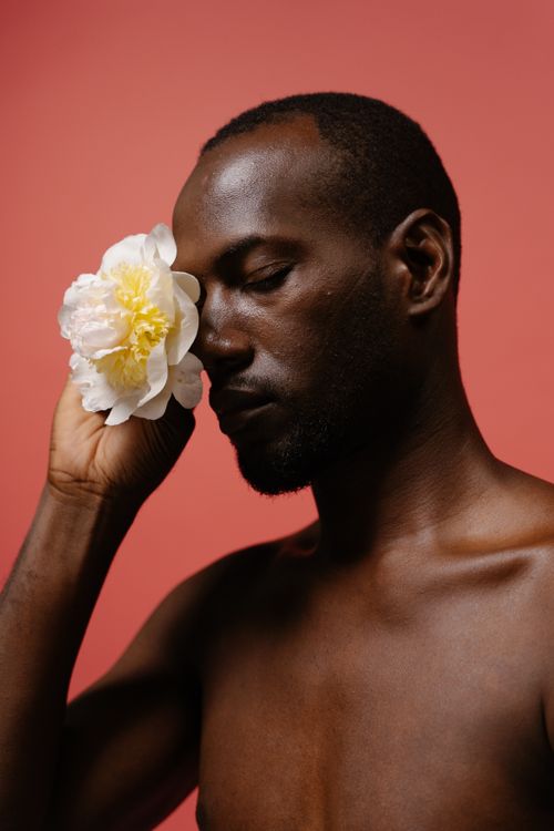 Free Shirtless man holding a white flower near eye against pink backdrop. Stock Photo