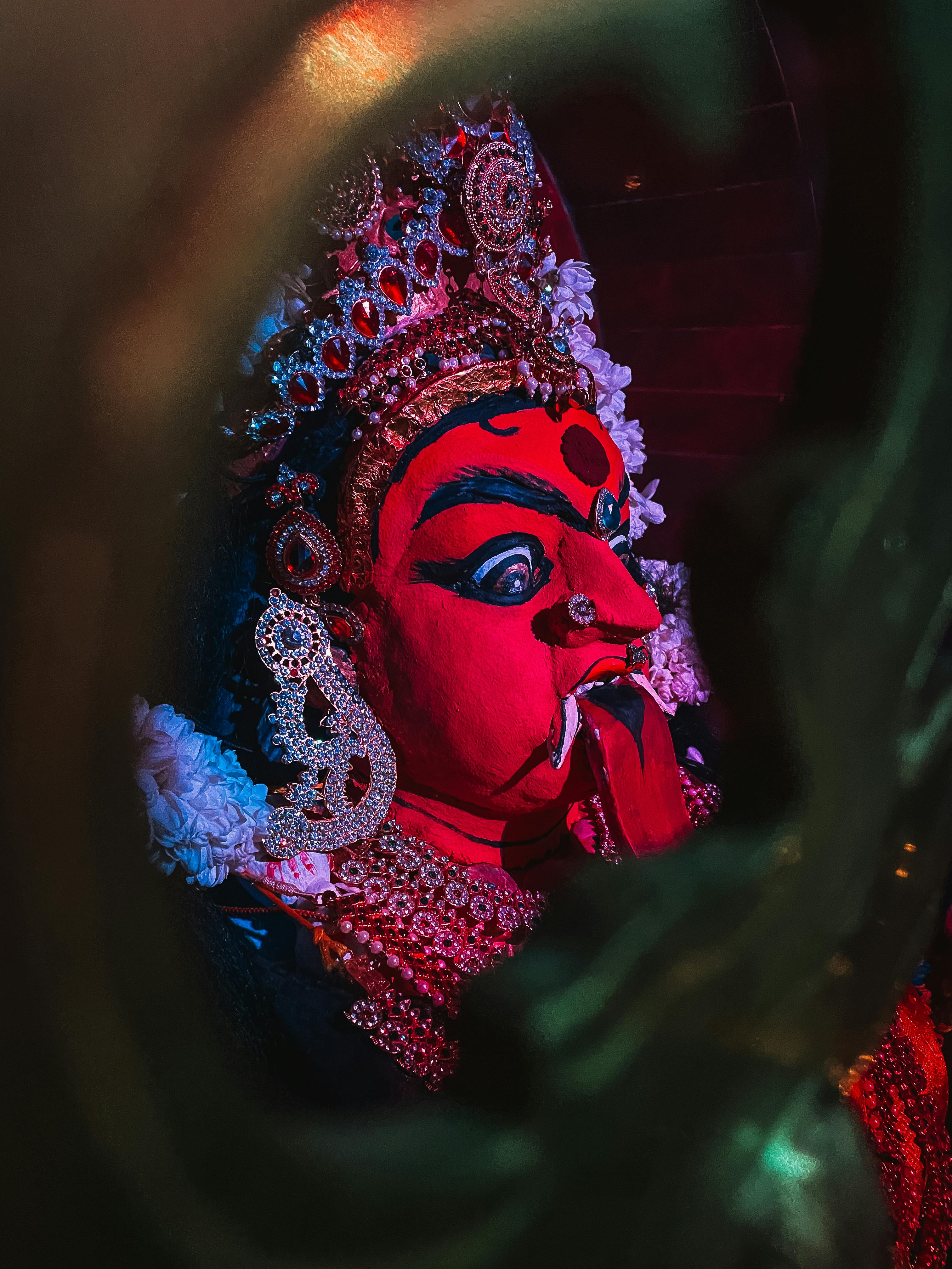 Close-up of a vividly decorated goddess statue with a red face and ornate jewelry, captured indoors.