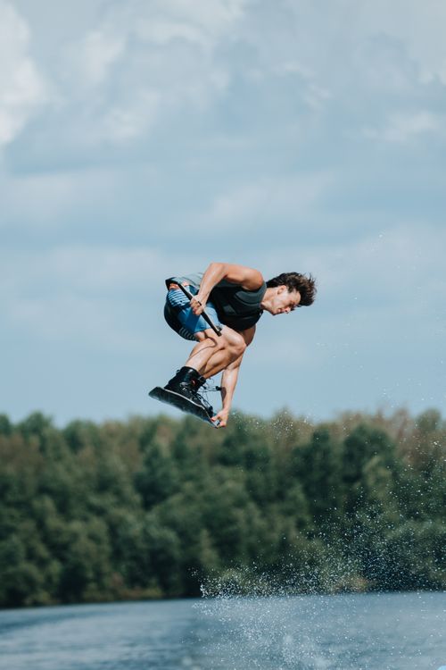 Free Man performing an impressive jump while wakeboarding on a lake, surrounded by forest. Stock Photo
