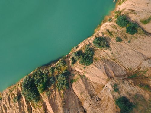 Free Aerial drone view of a rocky coastline meeting a vibrant body of water. Stock Photo