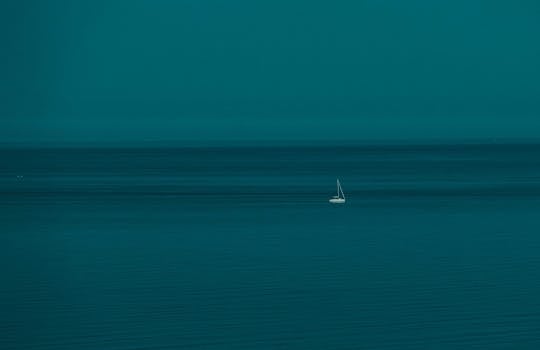 A single sailboat glides on a calm blue ocean under a vast sky, perfect for serene travel themes.