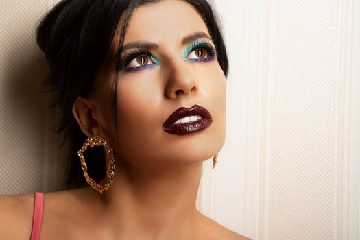 Close-up of a woman with dramatic makeup and earrings looking upwards, exuding glamour.