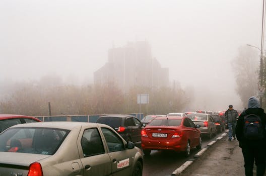 Vehicles lined up in a foggy traffic jam, city skyline barely visible.