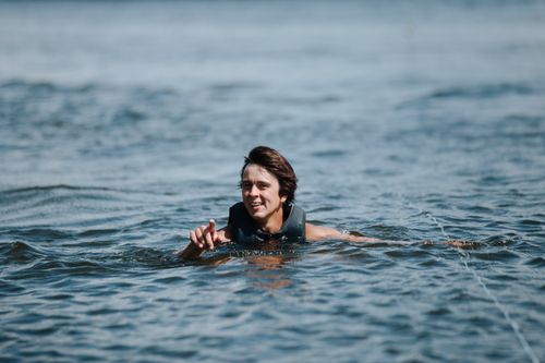 Free Man with brown hair swimming joyfully in a sunlit lake, capturing a vibrant summer moment outdoors. Stock Photo