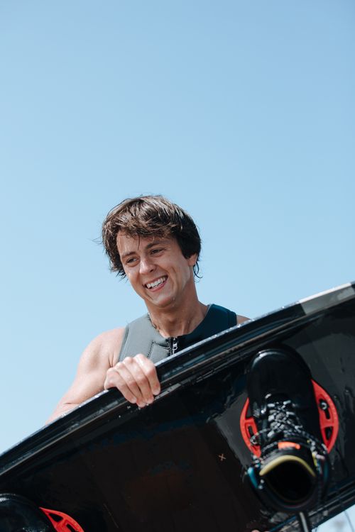 Free Smiling young man holding a wakeboard under a clear blue sky, enjoying a sunny outdoor adventure. Stock Photo