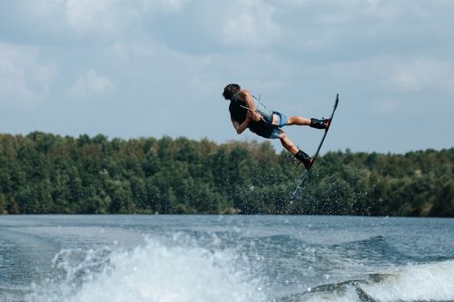 Free Wakeboarder executing a thrilling stunt over the water with a lush forest backdrop. Stock Photo