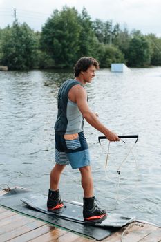 Young man preparing to wakeboard on a calm lake surrounded by greenery, showcasing outdoor adventure.