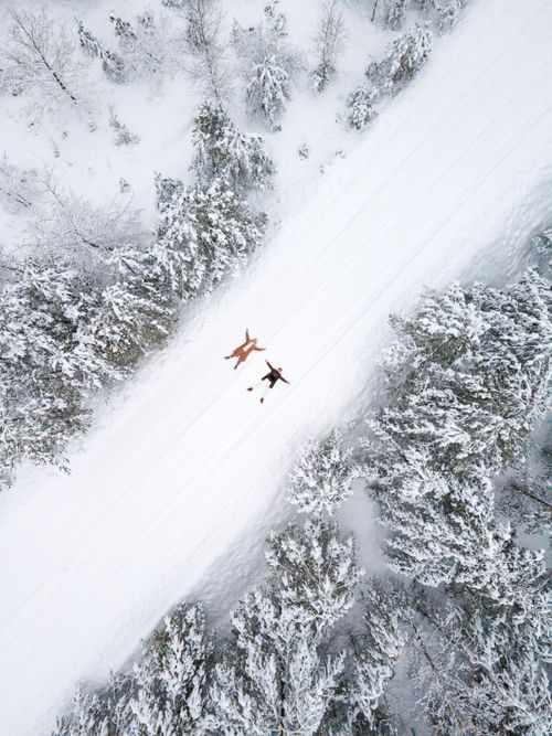 Free A drone captures a couple enjoying a snowy forest path creating snow angels. Stock Photo