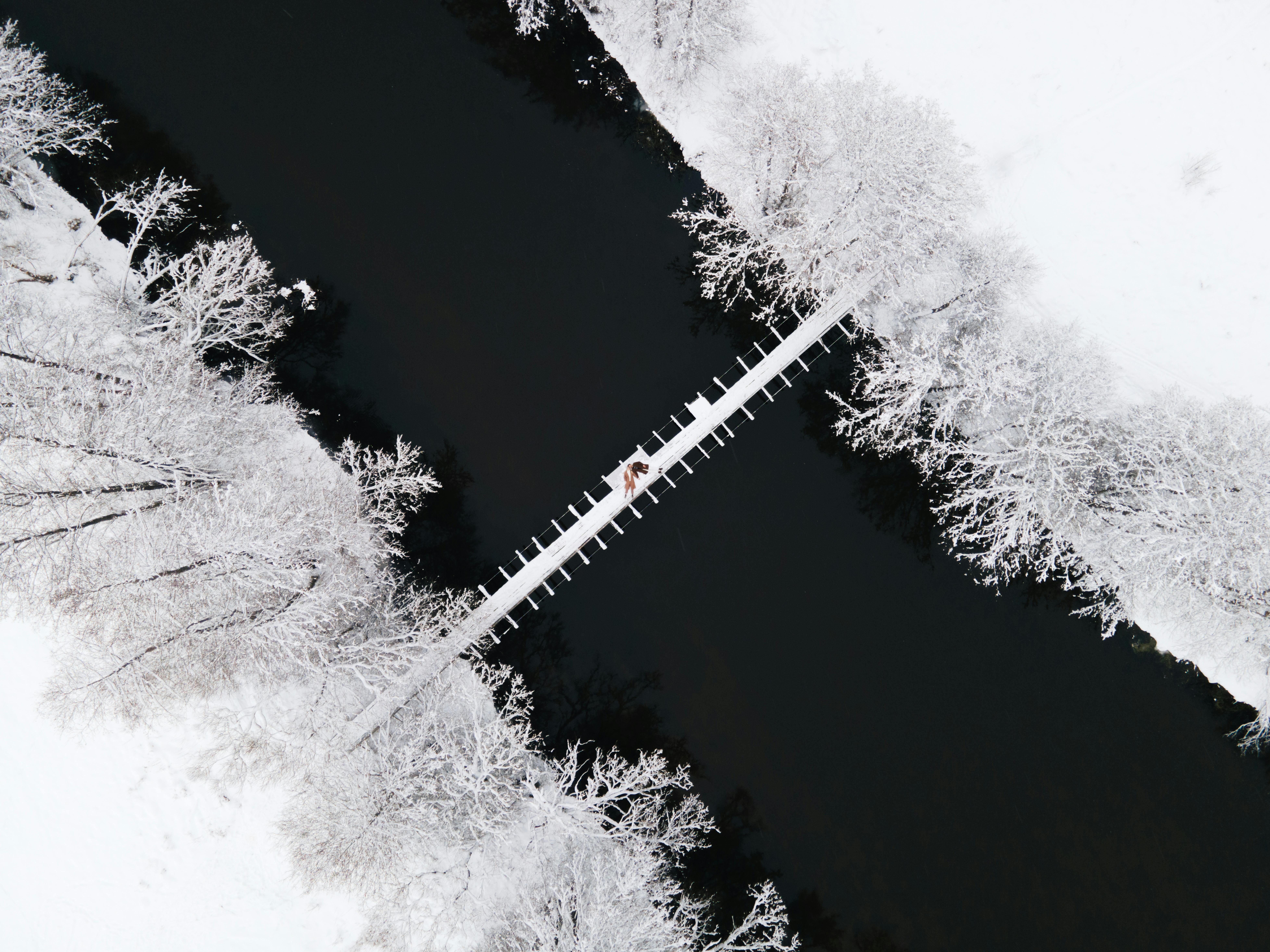 Drone shot capturing a couple lying on a wooden bridge surrounded by snowy landscape.