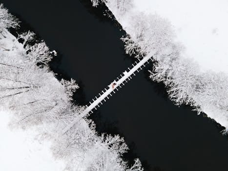 Drone shot capturing a couple lying on a wooden bridge surrounded by snowy landscape.