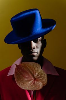 Stylish portrait of a man in a blue hat holding an anthurium against a vibrant background.