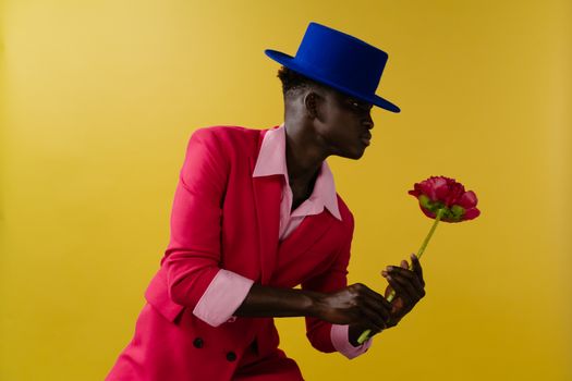 Fashionable man in vibrant outfit holding a carnation against a yellow background.