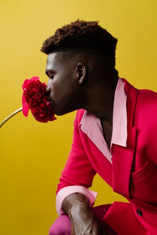 Free Side view of a modern adult man in red suit smelling a red flower. Stock Photo