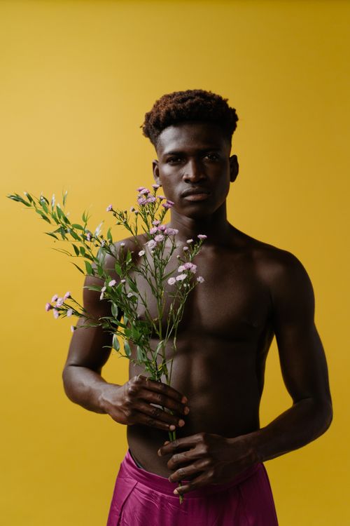Free A shirtless man holding a bouquet of flowers against a vibrant yellow background in a studio setting. Stock Photo