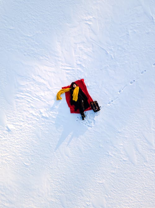 Woman in Coat and Yellow Scarf Lying on Red Blanket on Snow
